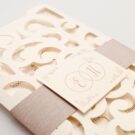 Λεπτομέρεια Φάκελος τρίπτυχος τρυπητός Lasercut 12,2 x 21,5 εκατ. μεταλλιζέ υπόλευκος και Κάρτα μεταλλιζέ υπόλευκη με φάσα λαμιναριστή λιλά 3,5x13 εκατ. και καρτάκι 5x6 εκατ.