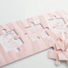 Προσκλητήριο Βάπτισης: Φάκελος τραβηχτός διάστασης 9,5x22 εκατ. με lazercut σε σχήμα puzzle, σε χαρτί δερματίνη ροζ 380γραμ. και Κάρτα σε χαρτί λείο ματ λευκό 250 γραμ. με εκτύπωση μελάνι δύο όψεων και θέμα σαλιάρα, όνομα και παπουτσάκια μωρού, πιπίλα και φορμάκι μωρού και κορδέλα γκρο ροζ με γαζί και καρτάκια σε σχήμα puzzle (3 τεμάχια) για όνομα προσκεκλημένων_Κωδικός 50655
