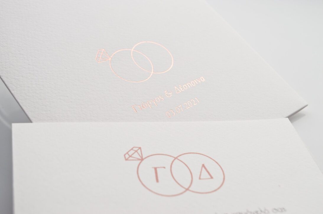 Λεπτομέρεια Προσκλητηρίου Γάμου: Φάκελος τραβηχτός διάστασης 14,5x20,5 εκατ. γκοφρέ (ανάγλυφο) μπιμπικωτό λευκό 250γραμ. και μονογράμματα σε θερμοτυπία ροζ χρυσό με θέμα βέρες, ονόματα ζευγαριού και ημερομηνία και Κάρτα σε χαρτί (ανάγλυφο) μπιμπικωτό λευκό 250 γραμ. με εκτύπωση μελάνι γκρι και ροζ χρυσό και θέμα βέρες, μονογράμματα και ημερομηνία _Κωδικός 0017