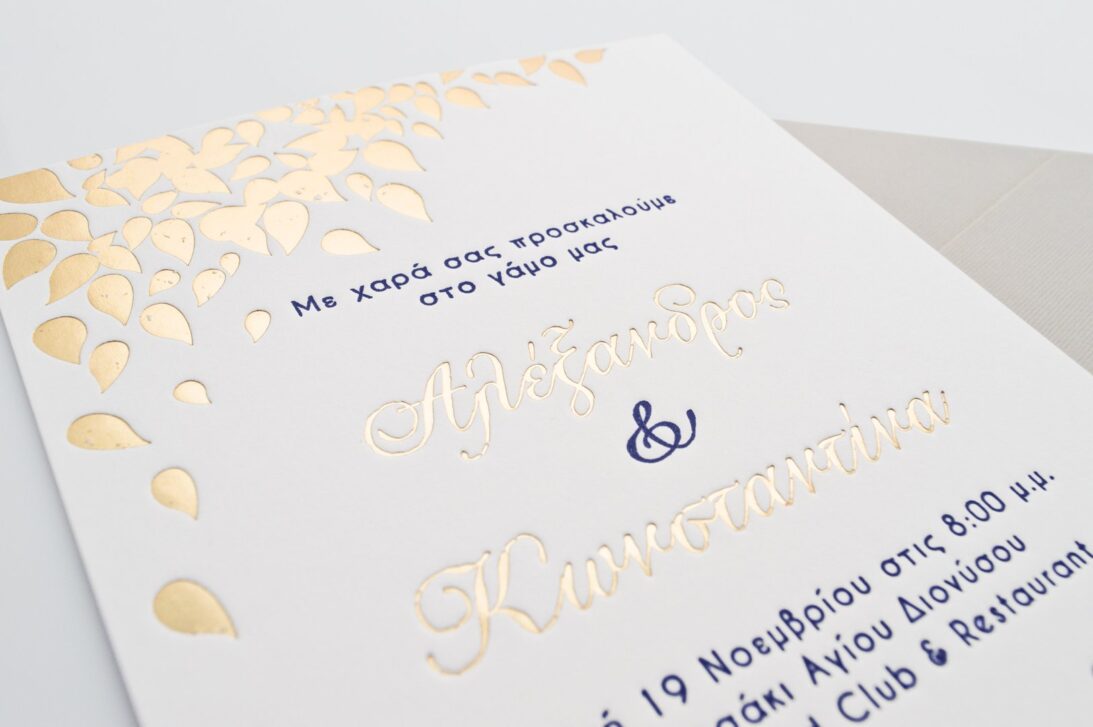 Λεπτομέρεια Προσκλητηρίου Γάμου: Φάκελος διάστασης 16x22 εκατ. σε χαρτί γκοφρέ γραμμωτό γκρι ανοικτό 160 γραμ. και Κάρτα σε χαρτί βαμβακερό λευκό 1000 γραμ. με εκτύπωση κειμένου σε βαθυτυπία (letterpress) σε χρώμα navy blue και χρυσό (χρυσοτυπία) και φύλλα σε βαθυτυπία χρυσοτυπία_Κωδικός ΓΝΣ 3034