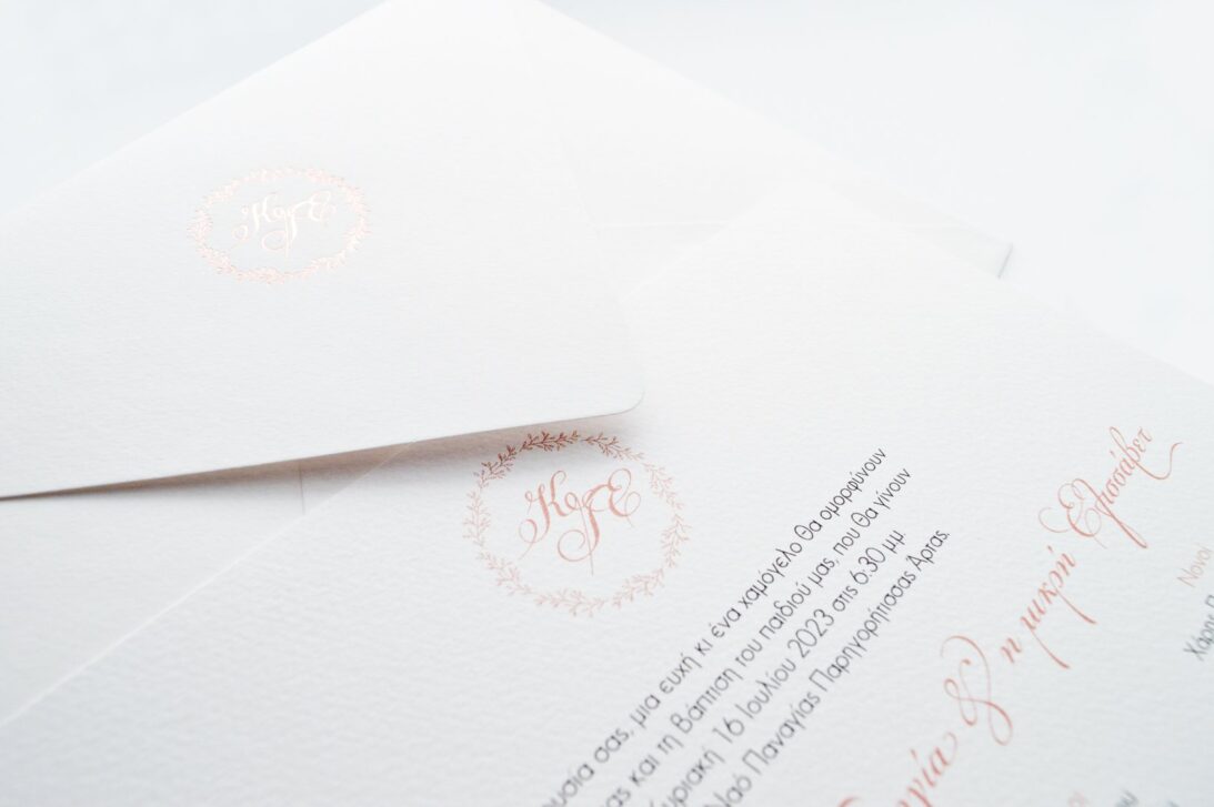 Λεπτομέρεια Προσκλητηρίου Γάμου και Βάπτισης: Φάκελος διάστασης 16x22 εκατ. σε χαρτί γκοφρέ μπιμπικωτό λευκό 150γραμ. με μοτίβο στεφανάκι και μονογράμματα σε εκτύπωση ροζ χρυσοτυπία και Κάρτα σε χαρτί γκοφρέ μπιμπικωτό λευκό 250 γραμ. με εκτύπωση μοτίβου στεφανάκι και μονογραμμάτων με μελάνι βρώμικο ροζ και κείμενο με εκτύπωση σε μελάνι γκρι και βρώμικο ροζ_Κωδικός_ΓΒΝΣ 2002