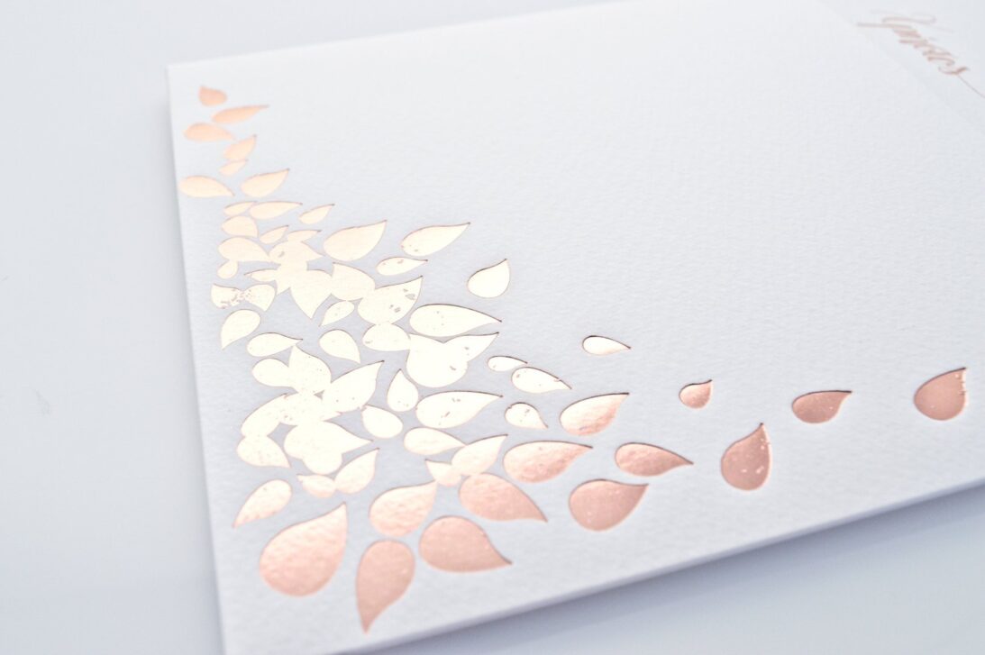 Λεπτομέρεια Προσκλητηρίου Γάμου: Φάκελος τραβηχτός διάστασης 15x15 εκατ. σε χαρτί γκοφρέ μπιμπικωτό 250 γραμ. και εκτύπωση θερμοτυπία ροζ χρυσό με θέμα φύλλα και Κάρτα διάστασης 22,5x15 εκατ. σε χαρτί γκοφρέ μπιμπικωτό λευκό 250 γραμ. με εκτύπωση μελάνι γκρι και ροζ χρυσό και θέμα δένδρο ζωής_Κωδικός ΓΝΣ 3038